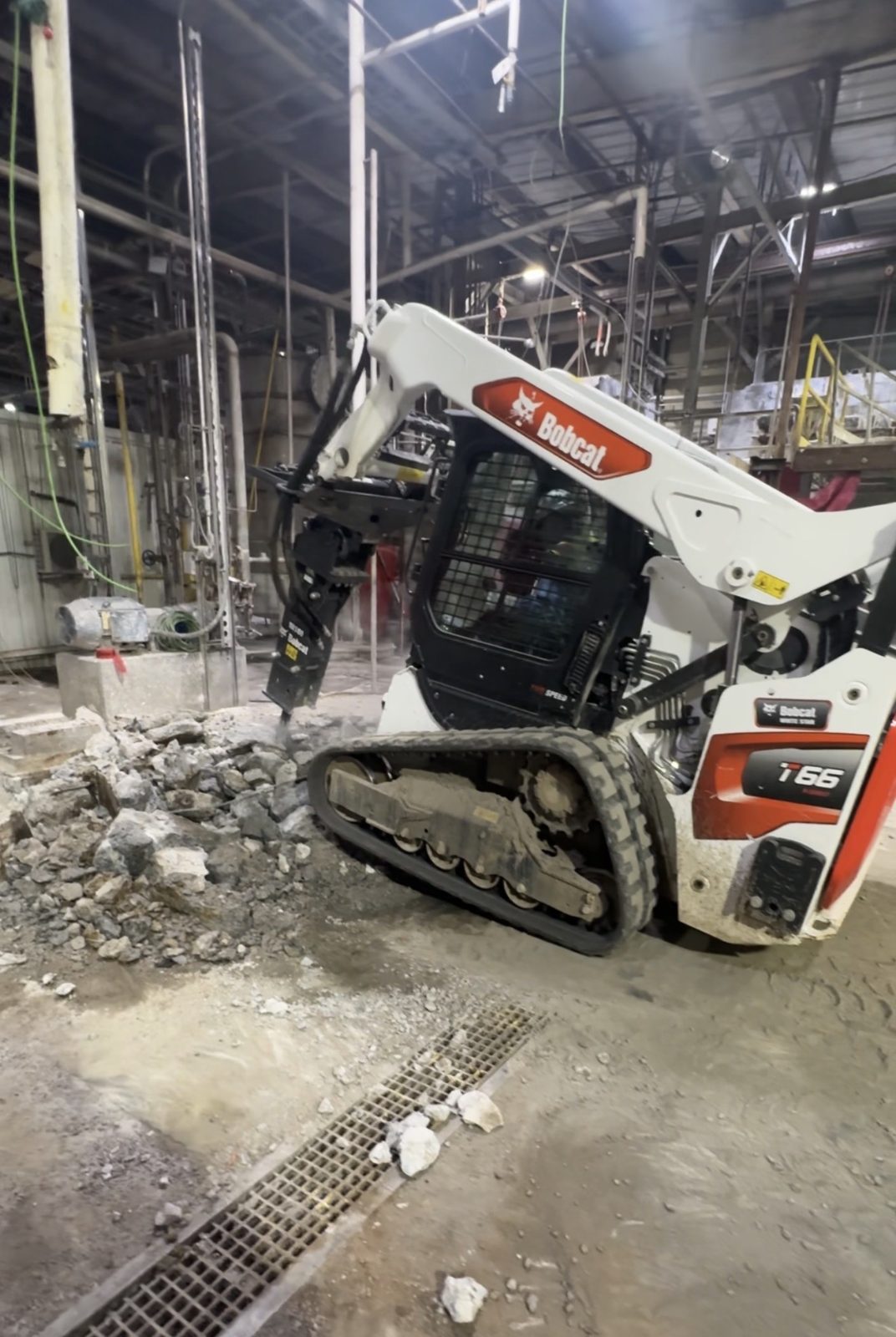 Bobcat breaking concrete inside industrial facility